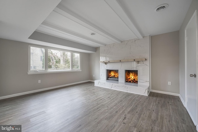 unfurnished living room with a high end fireplace, beamed ceiling, baseboards, and wood finished floors