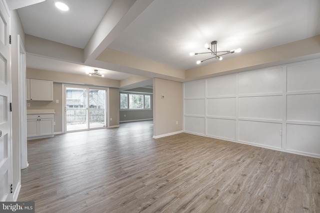 unfurnished living room with light wood-type flooring, a notable chandelier, and a decorative wall