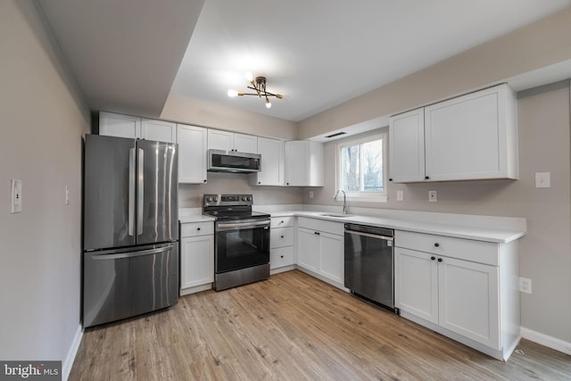 kitchen featuring stainless steel appliances, light countertops, light wood-style floors, white cabinets, and a sink