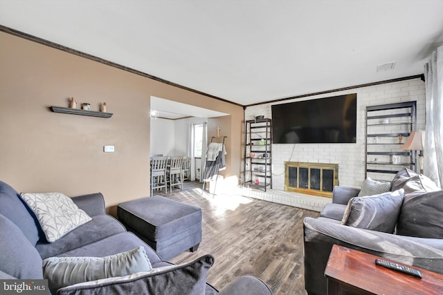 living room featuring ornamental molding, a brick fireplace, visible vents, and wood finished floors