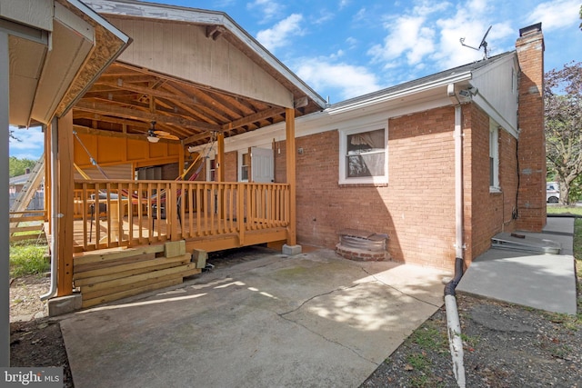 view of side of property featuring brick siding, a patio, a chimney, and a wooden deck