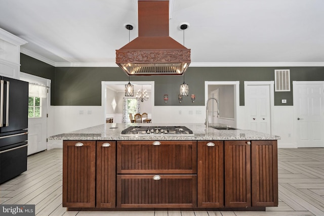 kitchen with wainscoting, island exhaust hood, high end black refrigerator, stainless steel gas cooktop, and a sink