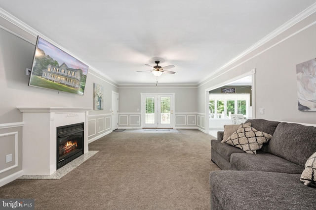 carpeted living room with a wainscoted wall, crown molding, a decorative wall, a fireplace with flush hearth, and a ceiling fan