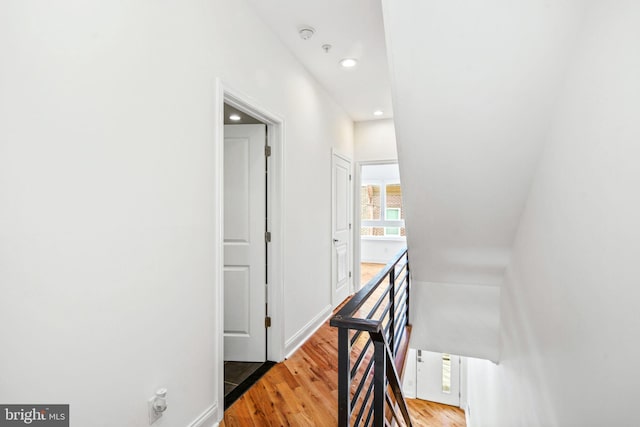 corridor with recessed lighting, wood finished floors, and an upstairs landing