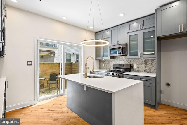 kitchen with decorative backsplash, gray cabinets, stainless steel appliances, light wood-style floors, and a sink