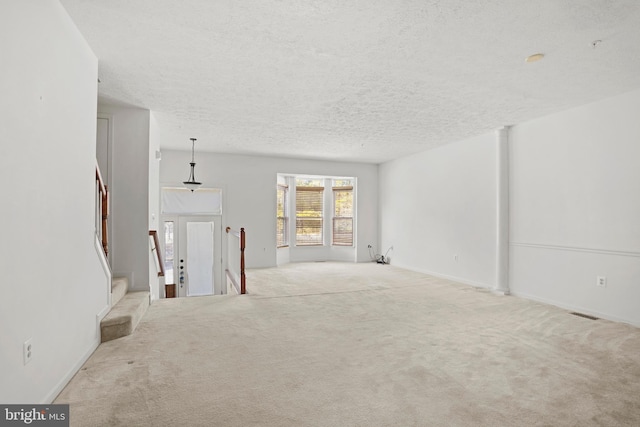 carpeted empty room featuring a textured ceiling and stairway