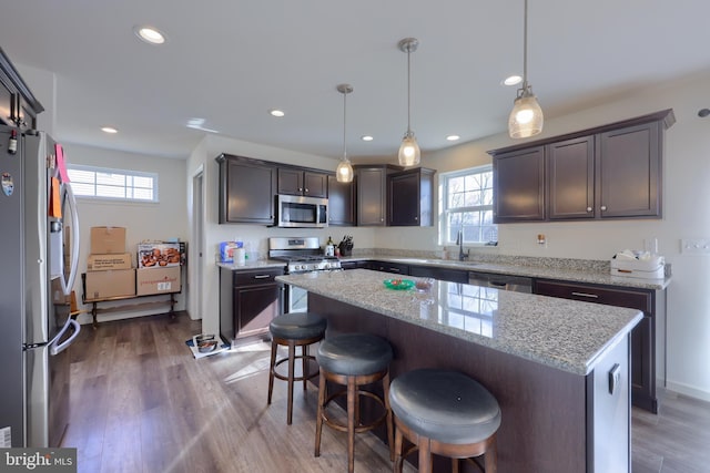 kitchen featuring stainless steel appliances, wood finished floors, a kitchen bar, and a wealth of natural light