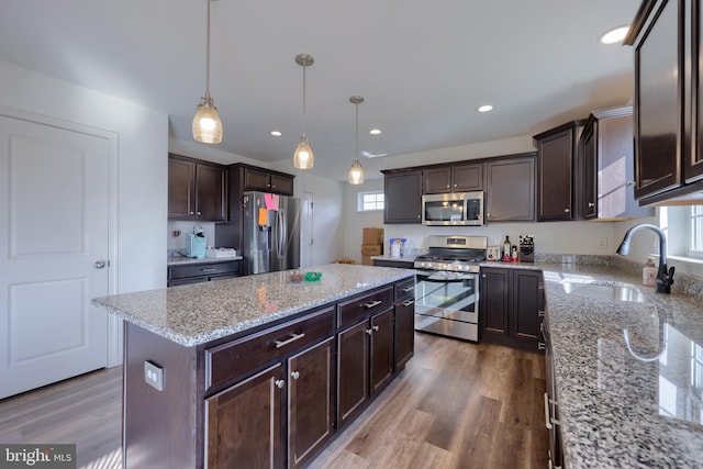 kitchen featuring light stone counters, wood finished floors, stainless steel appliances, dark brown cabinets, and a sink