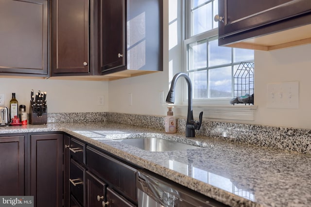 kitchen with light stone counters, dark brown cabinets, and a sink