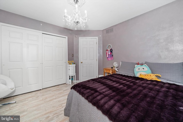 bedroom featuring light wood-style flooring, a closet, visible vents, and a notable chandelier