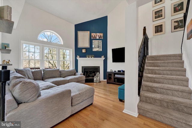 living area with light wood finished floors, a fireplace with flush hearth, stairs, and high vaulted ceiling