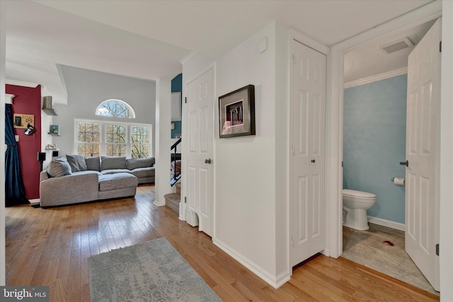 hallway with light wood-style flooring, visible vents, baseboards, stairway, and crown molding