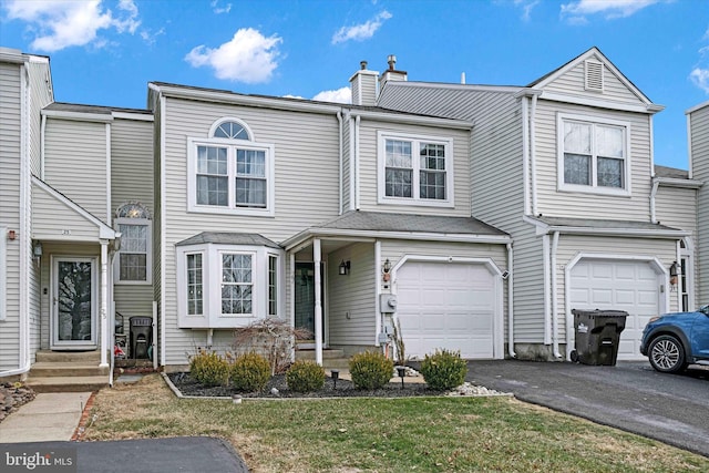 townhome / multi-family property featuring aphalt driveway, entry steps, a chimney, and a garage