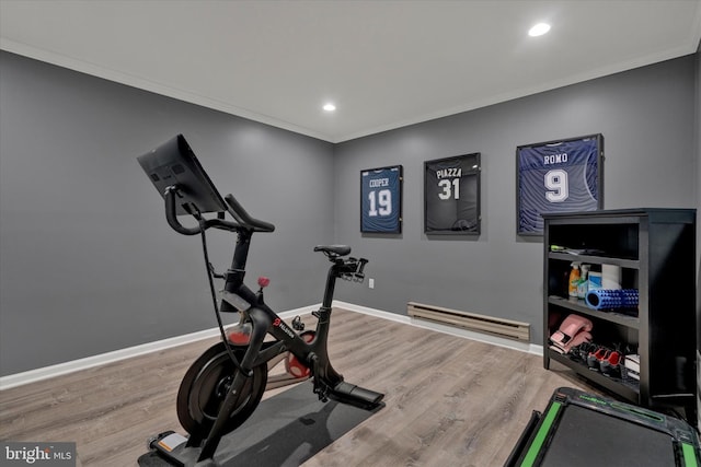 workout area with a baseboard heating unit, crown molding, baseboards, and wood finished floors