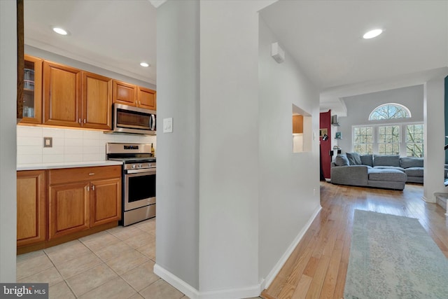 kitchen featuring baseboards, stainless steel appliances, brown cabinetry, and decorative backsplash