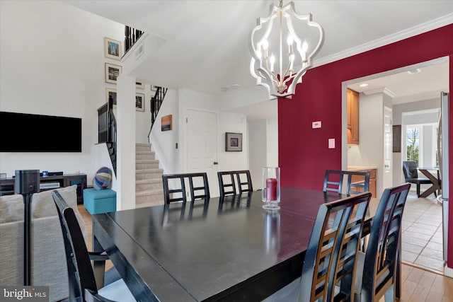 dining area with a notable chandelier, wood finished floors, visible vents, stairway, and crown molding