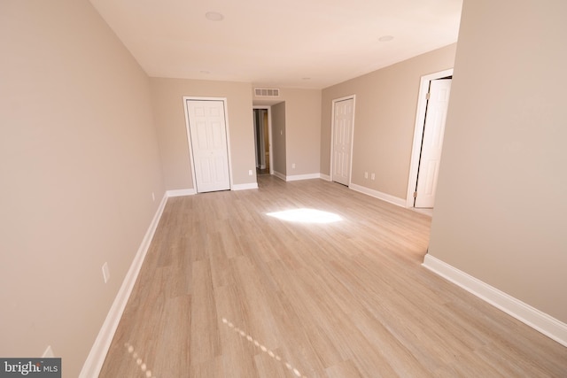 unfurnished bedroom featuring light wood-type flooring, baseboards, visible vents, and multiple closets