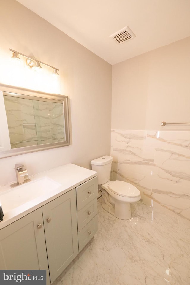 bathroom featuring toilet, a wainscoted wall, vanity, visible vents, and marble finish floor