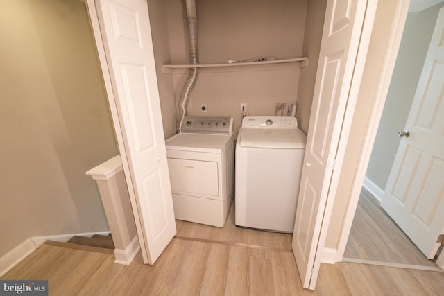 washroom with laundry area, baseboards, washer and clothes dryer, and light wood finished floors