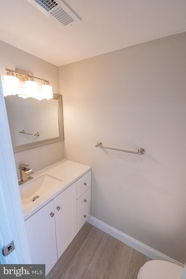 bathroom with toilet, wood finished floors, vanity, visible vents, and baseboards