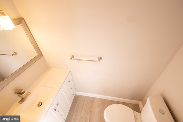 half bathroom featuring toilet, baseboards, wood finished floors, and vanity