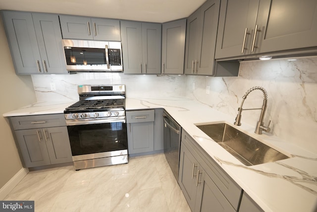 kitchen with light stone counters, gray cabinets, decorative backsplash, appliances with stainless steel finishes, and a sink