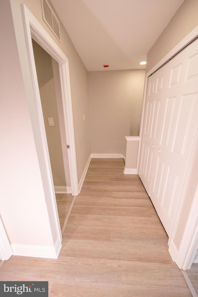 corridor with baseboards, visible vents, and light wood finished floors