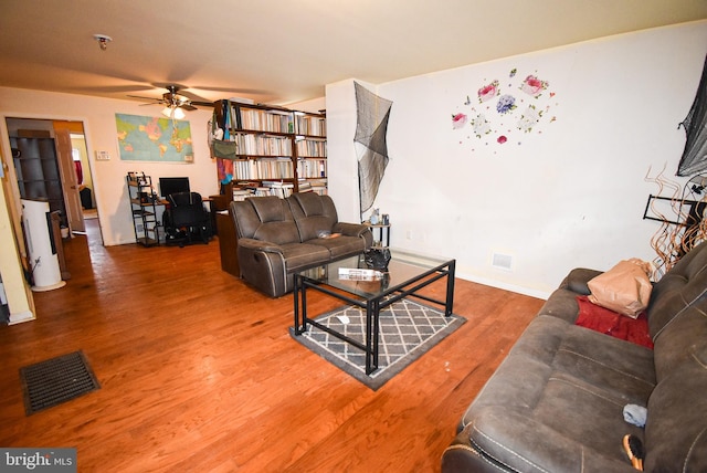 living area with baseboards, visible vents, a ceiling fan, wood finished floors, and gas water heater