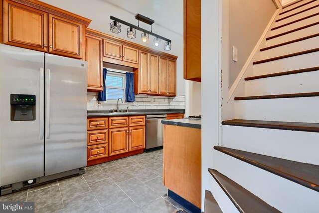 kitchen featuring appliances with stainless steel finishes, dark countertops, a sink, brown cabinets, and tasteful backsplash