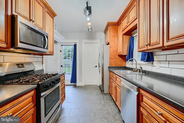 kitchen featuring stainless steel appliances, a sink, dark countertops, and decorative backsplash