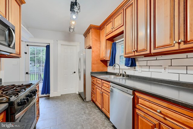 kitchen with stainless steel appliances, a sink, dark countertops, and brown cabinets