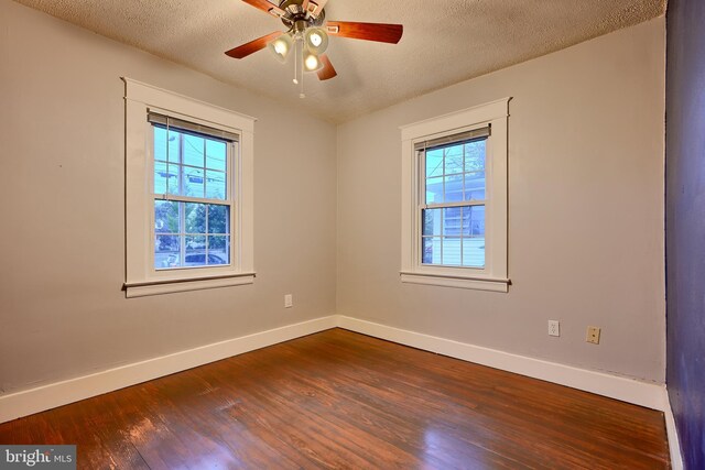 spare room featuring baseboards, dark wood-style flooring, a textured ceiling, and a ceiling fan
