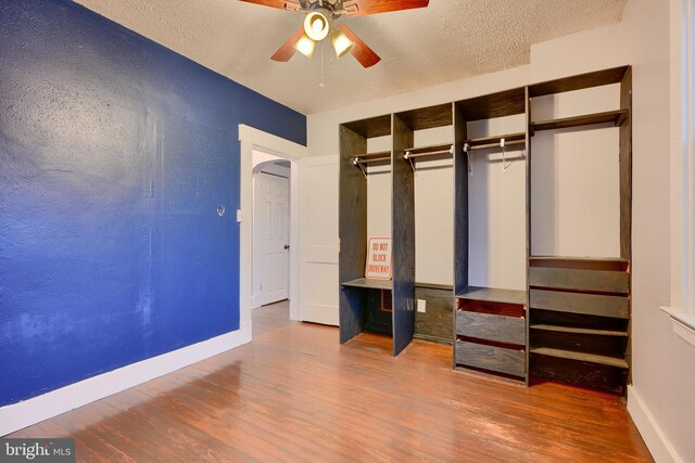 unfurnished bedroom featuring wood finished floors, baseboards, a textured ceiling, arched walkways, and a closet