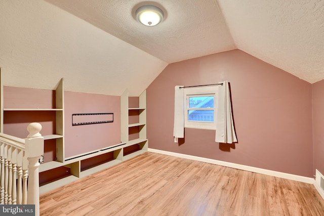 bonus room with a textured ceiling, wood finished floors, lofted ceiling, and baseboards