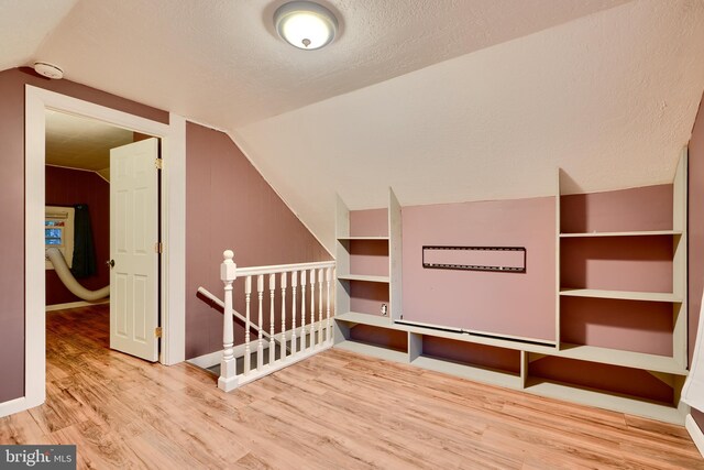 additional living space featuring wood finished floors, vaulted ceiling, a textured ceiling, and baseboards