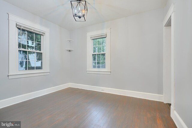 spare room with dark wood-style flooring, baseboards, and a chandelier