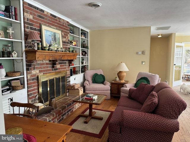 living room with a brick fireplace, visible vents, and wood finished floors