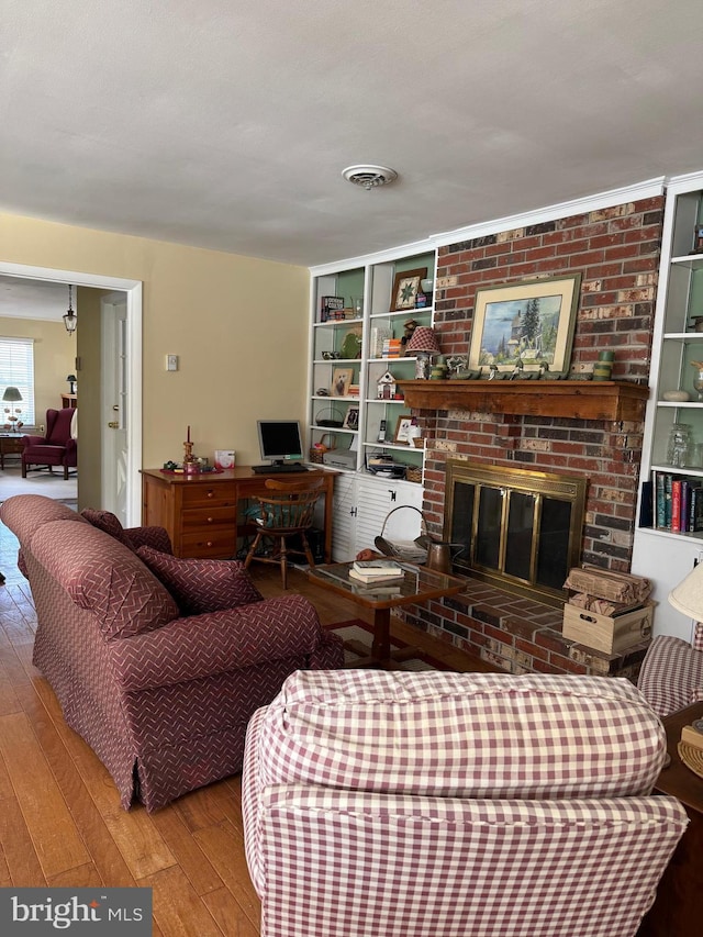 living area with visible vents, a brick fireplace, hardwood / wood-style flooring, and built in features