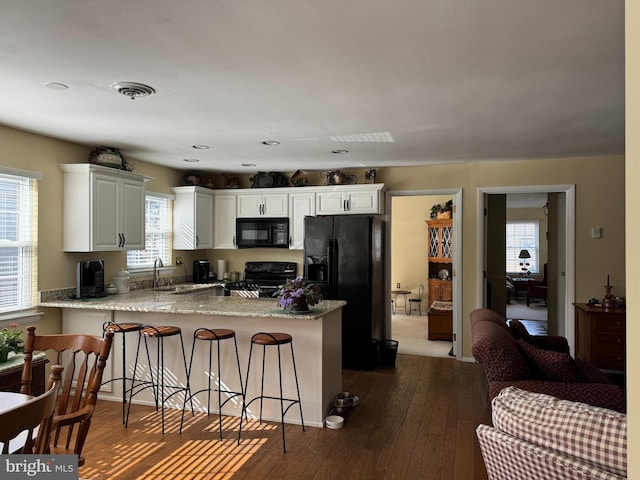 kitchen featuring a peninsula, a sink, white cabinetry, a kitchen breakfast bar, and black appliances