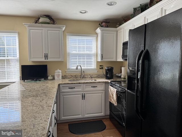 kitchen with a healthy amount of sunlight, black appliances, white cabinetry, and a sink