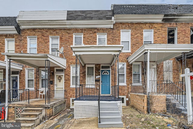 townhome / multi-family property with a shingled roof, covered porch, brick siding, and mansard roof