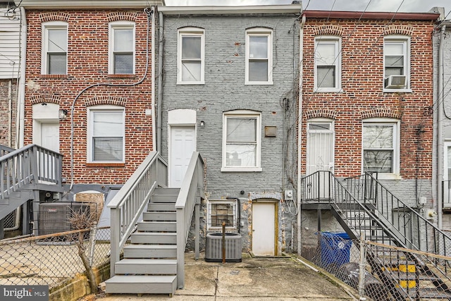 view of property with central AC unit, cooling unit, fence, and brick siding