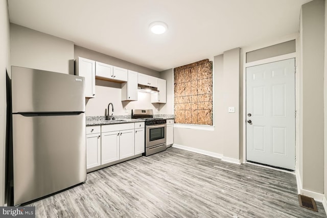 kitchen with appliances with stainless steel finishes, white cabinets, a sink, and under cabinet range hood