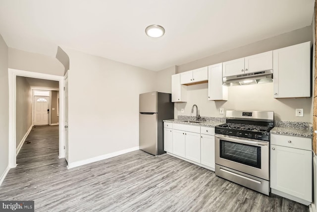 kitchen featuring light wood finished floors, white cabinets, stainless steel appliances, under cabinet range hood, and a sink