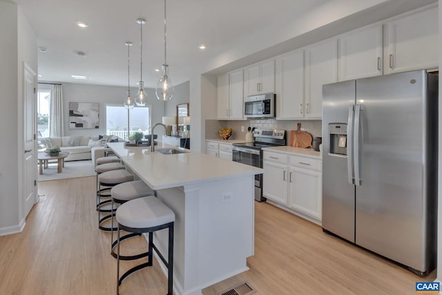 kitchen with white cabinetry, stainless steel appliances, a sink, and open floor plan