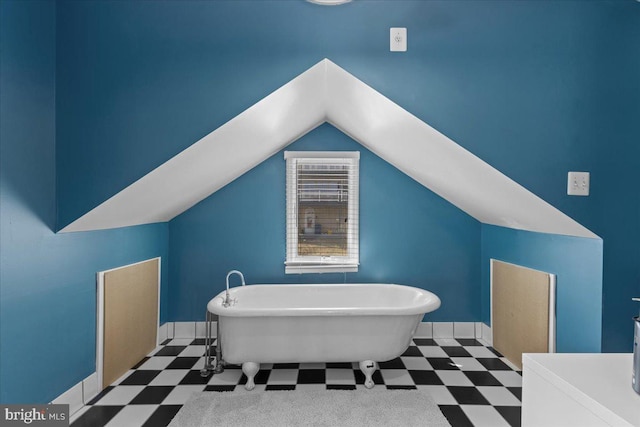 bathroom with lofted ceiling, baseboards, a freestanding bath, and tile patterned floors