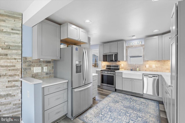 kitchen featuring stainless steel appliances, light wood-style floors, light countertops, gray cabinets, and decorative backsplash