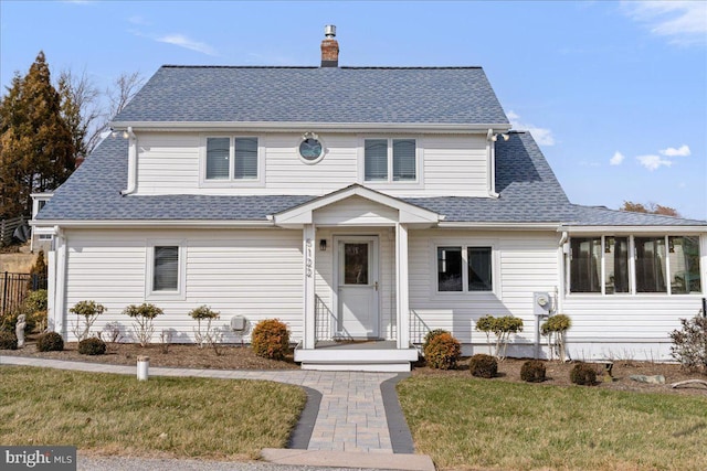 traditional-style home featuring roof with shingles, fence, a chimney, and a front lawn