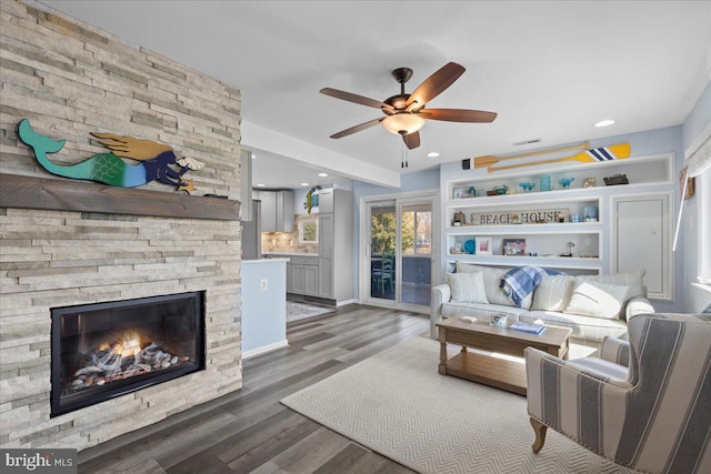 living area with visible vents, a ceiling fan, wood finished floors, a stone fireplace, and recessed lighting