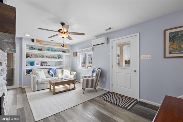 living room with ceiling fan, a wall mounted AC, wood finished floors, and baseboards